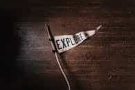 Artistic flat lay of an 'Explore' pennant on rustic wooden flooring, emphasizing adventure and exploration.
