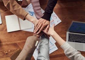 Diverse professionals unite for teamwork around a wooden table with laptops and documents.