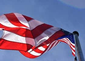 Close-up of a waving American flag under clear blue skies, symbolizing freedom and patriotism.