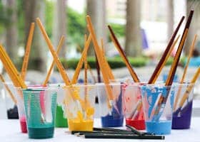Vibrant paint brushes and pencils in plastic cups for arts and crafts.
