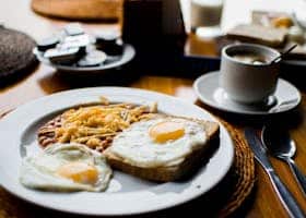 A hearty breakfast with fried eggs, baked beans, and toast served with coffee in a cozy setting.