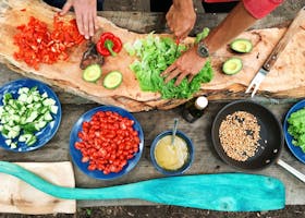 Fresh ingredients being prepared on a rustic wooden table, showcasing vibrant vegetables and hands at work.
