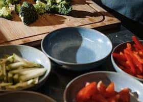 A chef chops broccoli on a cutting board surrounded by fresh vegetables in a kitchen setting.