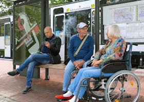 Adults and a senior in a wheelchair waiting at a bus stop in Germany.
