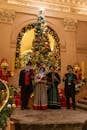 Victorian-dressed carolers perform by an ornate Christmas tree indoors.